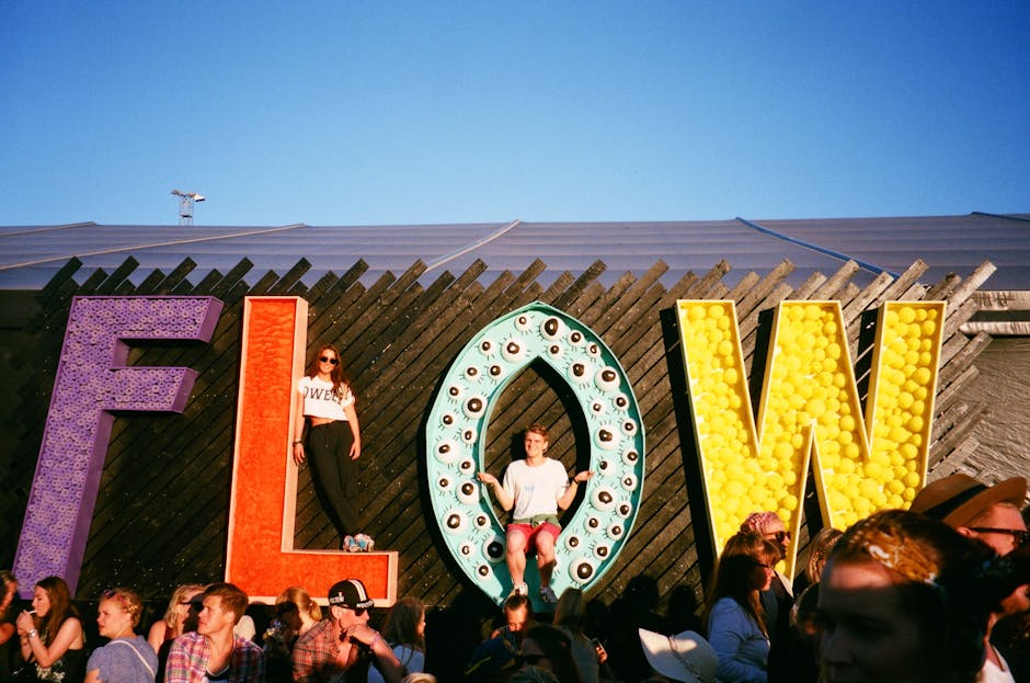 People enjoying a lively festival with colorful FLOW sign as backdrop.